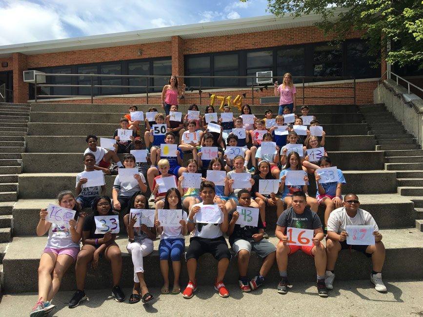 Teachers Tracey McManus and Emily Lohse with their students who are holding signs with the number of books they read this year.