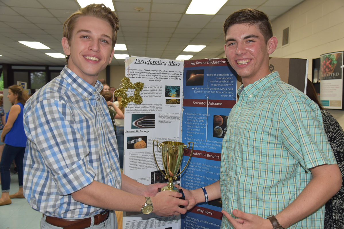 Research partners John Panos and Matthew Gennarelli stand near a summary of their work 