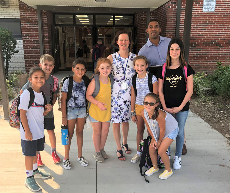 Woodhull Principal Lara Gonzalez and Student Dean Julian Watts with a group of students near the main entrance.