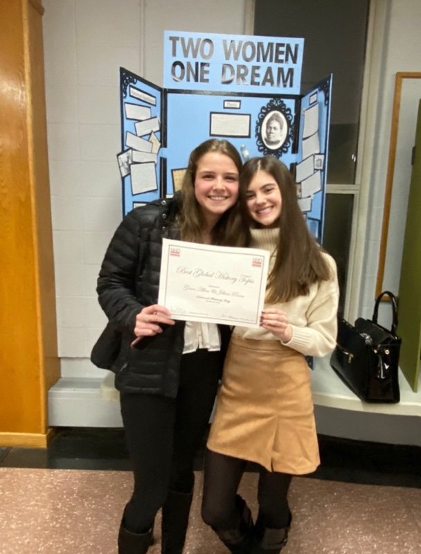 Jillian Panos and Grace Allen with their award certificate in front of the exhibit.