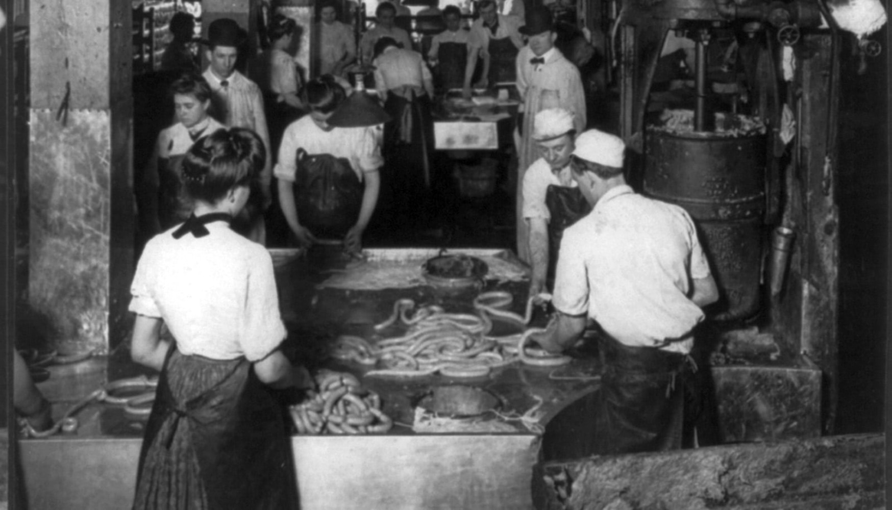 Meatpacking industry workers making link sausages in less than ideal conditions.